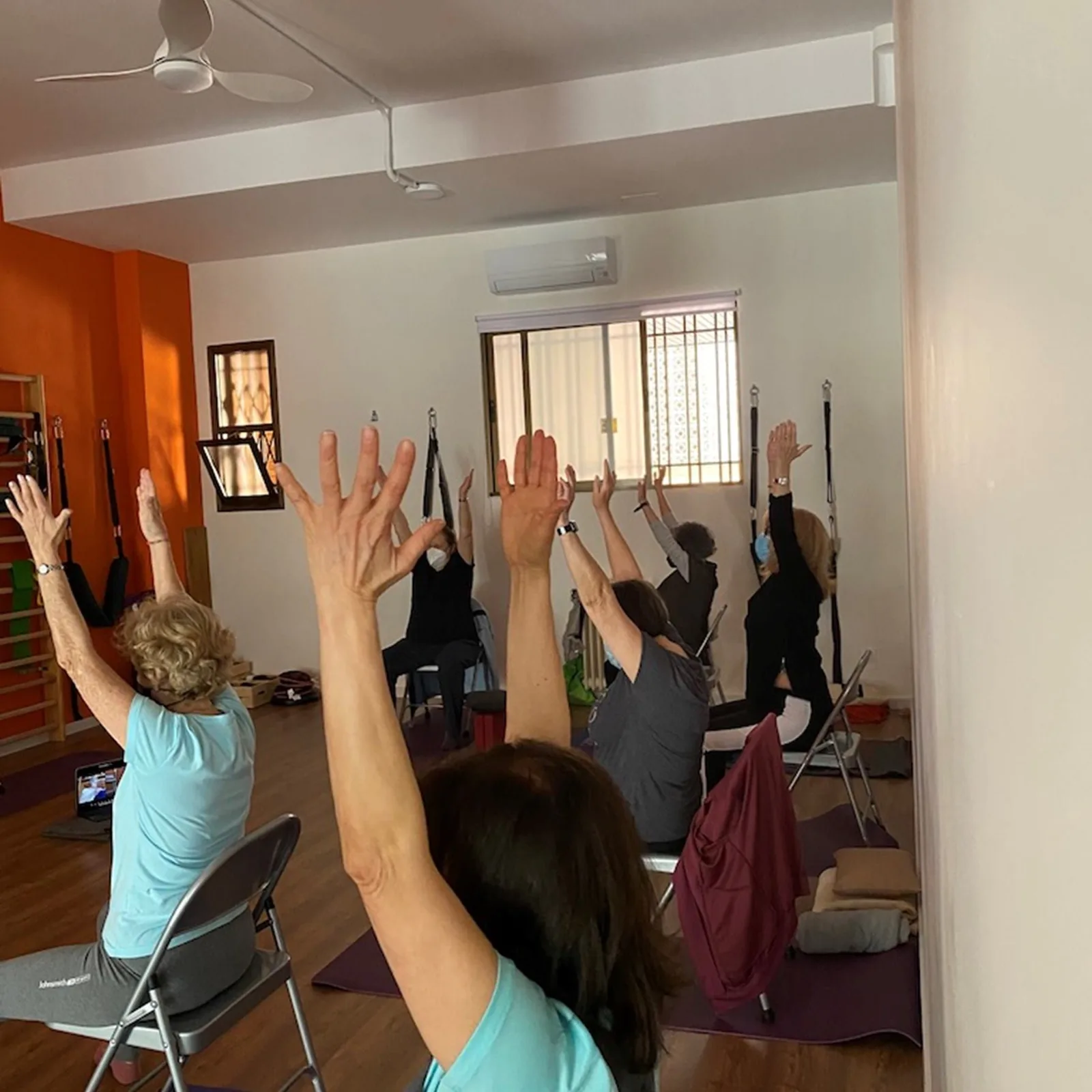Alumnas con los brazos en alto durante la clase de yoga para mayores